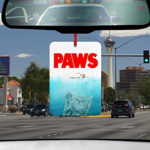Könnte beinhalten: Ein weißer Auto-Lufterfrischer mit einem blauen und weißen Bild einer Katze mit dem Wort "PAWS" in roten Buchstaben.