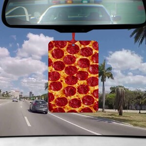 May include: A car air freshener with a pepperoni pizza design. The air freshener is hanging from the rearview mirror of a car.