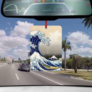 May include: A car air freshener featuring a print of "The Great Wave off Kanagawa" by Katsushika Hokusai. The print is in a traditional Japanese style with blue, white, and gray colors.