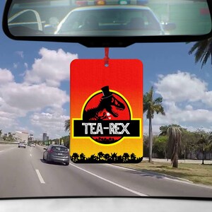 May include: A red, yellow and black car air freshener featuring a cartoon dinosaur wearing a top hat and holding a teacup. The text "TEA-REX" is printed on the air freshener.