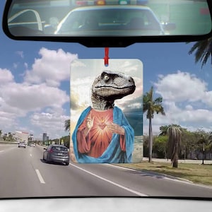 Könnte beinhalten: Ein Auto-Lufterfrischer mit einem humorvollen Bild eines Velociraptors, der als Jesus Christus verkleidet ist. Das Bild ist vor einem blauen Himmel mit weißen Wolken platziert. Der Lufterfrischer ist rechteckig und hat eine rote Schnur, die von oben hängt.