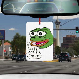 Könnte beinhalten: Ein weißer Auto-Lufterfrischer mit einem grünen Comic-Frosch mit dem Text "feels good man" in einer Sprechblase.