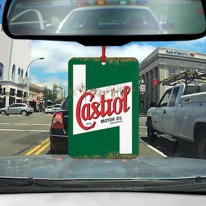 Op de afbeelding: Een groene en witte autoluchtverfrisser met een vintage Castrol Motor Oil-logo. Het logo is rood en wit met het woord "Castrol" in een gestileerd lettertype. De luchtverfrisser hangt aan een achteruitkijkspiegel in een auto.