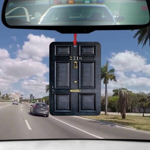 Könnte beinhalten: Schwarzer Auto-Lufterfrischer in Form einer Tür mit der Nummer 221B. Die Tür hat einen Türklopfer aus Messing und eine Messing-Namensschilder mit der Aufschrift "Sherlock".