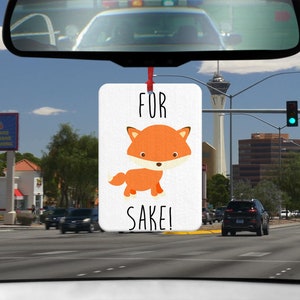 Könnte beinhalten: Ein weißer Auto-Lufterfrischer mit einer roten Schnur, die von oben hängt. Der Lufterfrischer hat einen orangefarbenen Comic-Fuchs darauf und den Text "FOR SAKE!"
