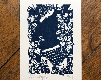May include: A blue and white linocut print of a person standing in a garden. The print is titled "Mai" and dated "8/21".