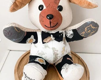 May include: A handmade memory bear crafted from various patterned fabrics, including black cloth with egg and milk carton prints, and white fabric with character illustrations. It features black button eyes, a black nose, and a black bowtie.