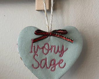May include: A light blue heart-shaped ornament with a red and green ribbon and the embroidered text "Ivory Sage".