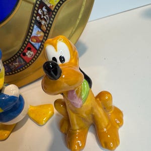 May include: A set of three ceramic Disney character figurines. The figurines are of Mickey Mouse, Donald Duck, and Goofy. The figurines are painted in their signature colors and have a glossy finish.