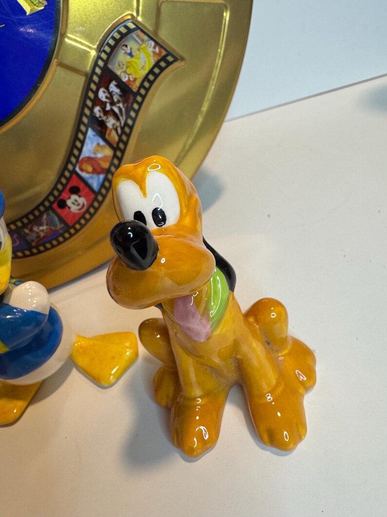 May include: A set of three ceramic Disney character figurines. The figurines are of Mickey Mouse, Donald Duck, and Goofy. The figurines are painted in their signature colors and have a glossy finish.