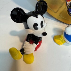 May include: A black and white ceramic figurine of Mickey Mouse sitting with his legs crossed. He is wearing red shorts and yellow shoes.
