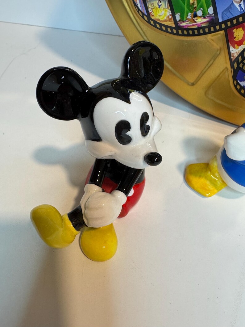 May include: A black and white ceramic figurine of Mickey Mouse sitting with his legs crossed. He is wearing red shorts and yellow shoes.