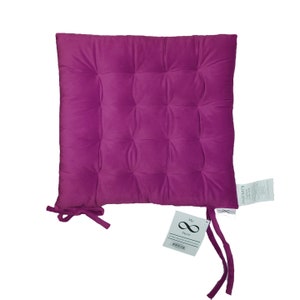 May include: A deep purple, square-shaped chair cushion with tufted buttons and ties. The cushion has a tag attached that says "My Store" with an infinity symbol.