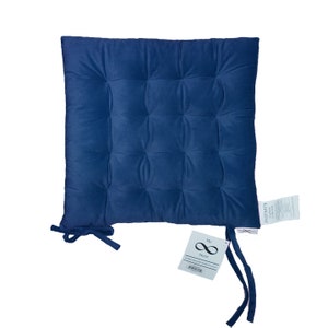 May include: A square, navy blue cushion with a tufted design. The cushion has ties on two corners and a tag that reads "My Store" with a website address. A second tag reads "INFINITY Cotton Cushions".