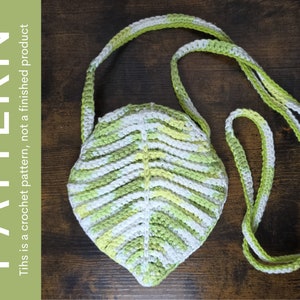 Puede incluir: Un bolso de ganchillo con forma de hoja en colores verde, blanco y amarillo. El bolso tiene una correa larga para llevarlo al hombro.