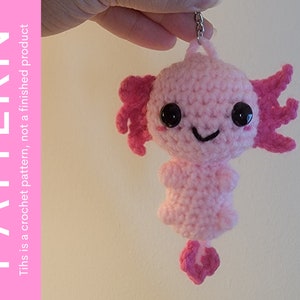 May include: Pink crocheted axolotl keyring with black eyes and a smiling mouth. The axolotl is hanging from a silver chain.
