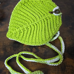 May include: A green crocheted leaf-shaped bag with a white and green crocheted strap. The bag has a small key charm attached to it.