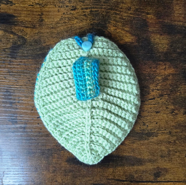 May include: A green crocheted leaf-shaped pouch with a blue and green crocheted strap and a blue button.
