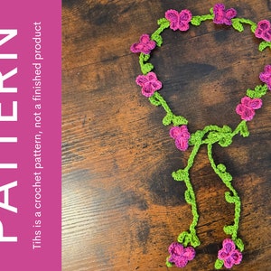 Könnte beinhalten: Eine gehäkelte Halskette mit rosa Blüten und grünen Blättern. Die Halskette hat die Form eines Kreises mit einem langen, herabhängenden Strang.