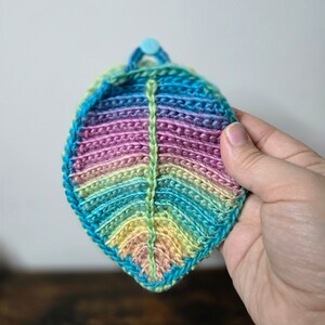 May include: A crocheted leaf-shaped dishcloth in shades of blue, green, pink, and yellow.