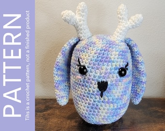 May include: A crocheted stuffed animal shaped like a deer with white antlers, blue, purple, and yellow yarn, and black eyes.