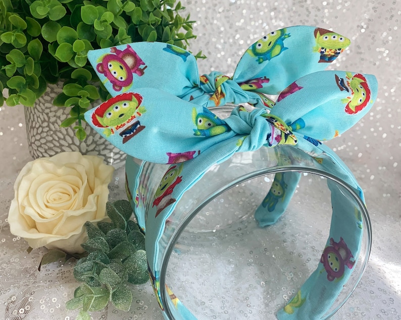 May include: A light blue headband with a bow, featuring a repeating pattern of green alien characters from the Toy Story franchise.