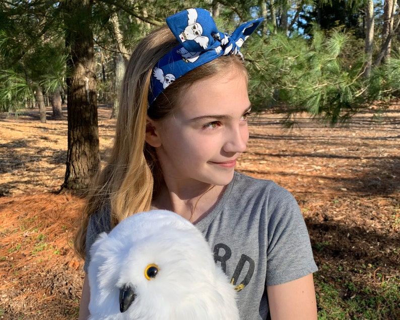 May include: A young person wearing a blue headband with a white owl pattern and a grey shirt with the word "Bird" on it. They are holding a white stuffed owl with yellow eyes.