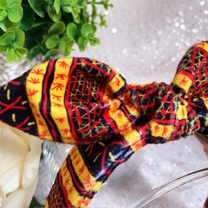 Peut inclure: Un bandeau jaune, rouge et noir &agrave; motif avec un n&oelig;ud. Le bandeau est fait d'un tissu doux et duveteux.