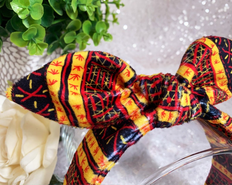Peut inclure: Un bandeau jaune, rouge et noir &agrave; motif avec un n&oelig;ud. Le bandeau est fait d'un tissu doux et duveteux.