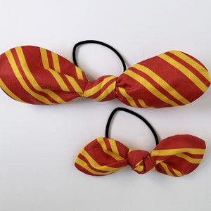May include: Two red and yellow striped fabric hair ties. The larger hair tie is tied in a bow and the smaller hair tie is tied in a bow.