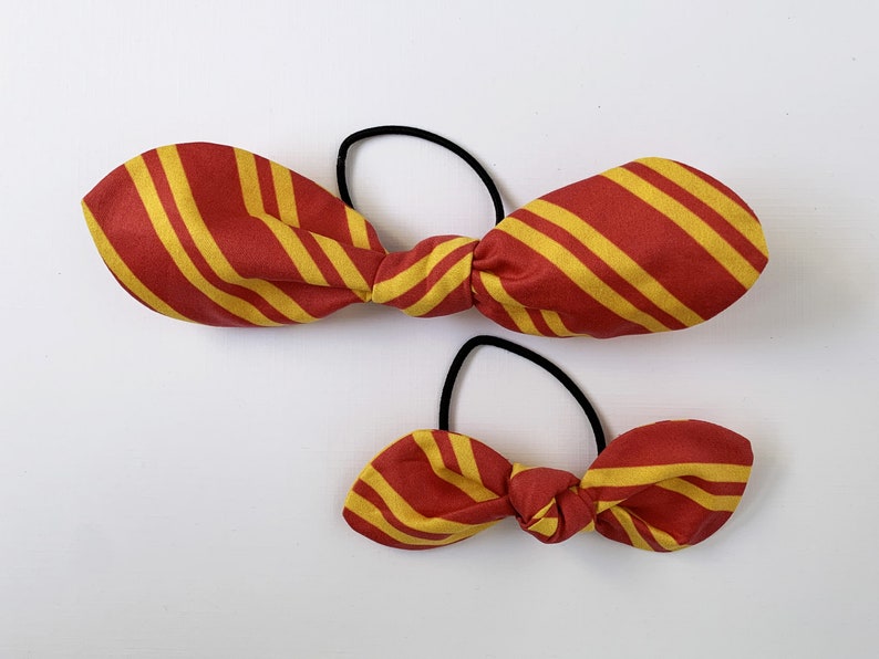 May include: Two red and yellow striped fabric hair ties. The larger hair tie is tied in a bow and the smaller hair tie is tied in a bow.