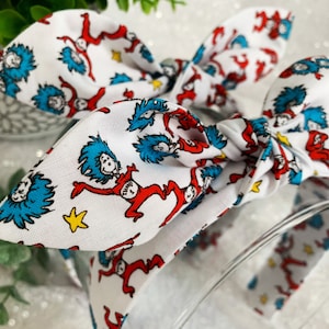 May include: A white headband with a red and blue print of the character Thing 1 from the book "The Cat in the Hat".
