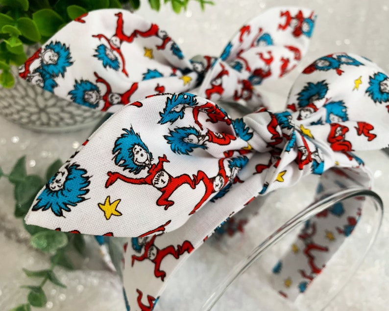 May include: A white headband with a red and blue print of the character Thing 1 from the book "The Cat in the Hat".