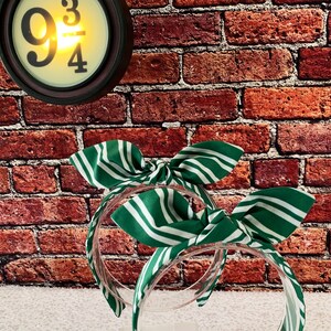 May include: Two green and white striped headbands with bow details. The headbands are clear plastic. A round clock with the text "9 3/4" is in the background.