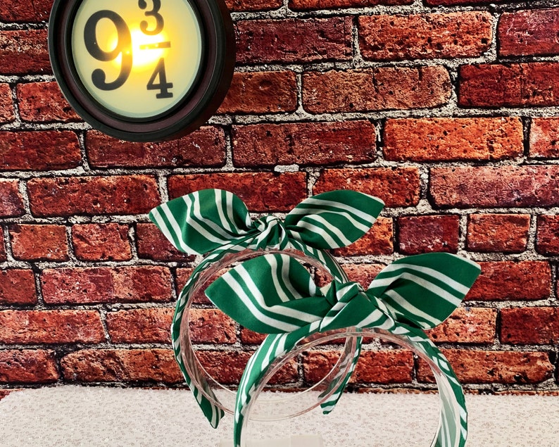 May include: Two green and white striped headbands with bow details. The headbands are clear plastic. A round clock with the text "9 3/4" is in the background.