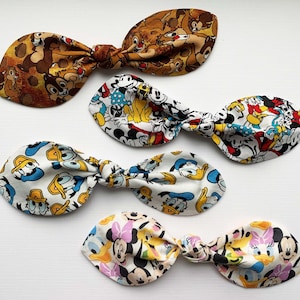 May include: Four fabric hair bows featuring different Disney character prints. The bows are tied in a knot and have a brown, white and blue colour scheme.