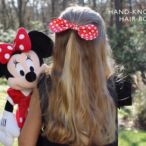 K&ouml;nnte beinhalten: Ein junges M&auml;dchen mit langen blonden Haaren tr&auml;gt ein rotes und wei&szlig;es gepunktetes Haarband. Das Band ist handgekn&uuml;pft. Das M&auml;dchen h&auml;lt ein Pl&uuml;sch-Minnie-Maus-Spielzeug.