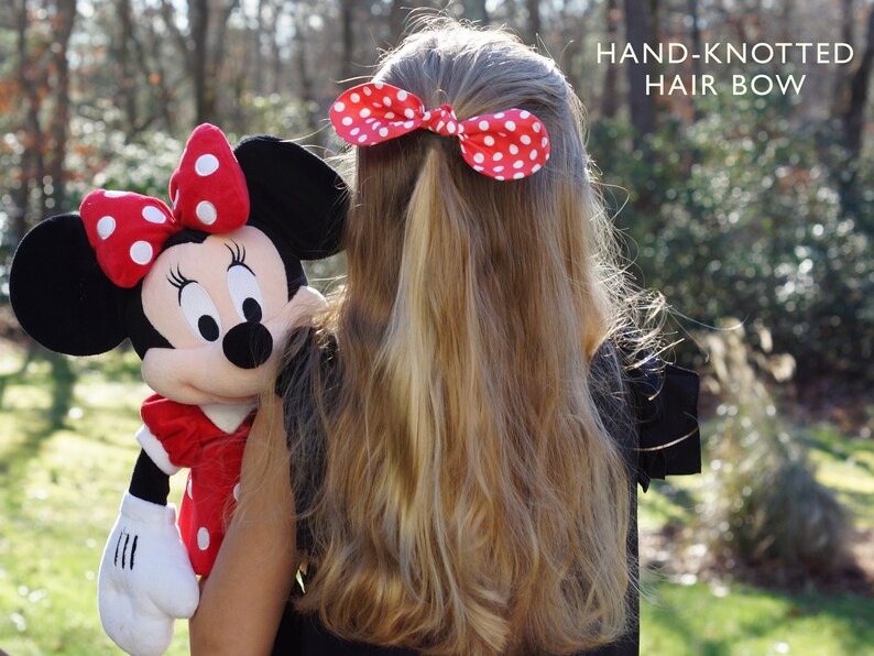 K&ouml;nnte beinhalten: Ein junges M&auml;dchen mit langen blonden Haaren tr&auml;gt ein rotes und wei&szlig;es gepunktetes Haarband. Das Band ist handgekn&uuml;pft. Das M&auml;dchen h&auml;lt ein Pl&uuml;sch-Minnie-Maus-Spielzeug.