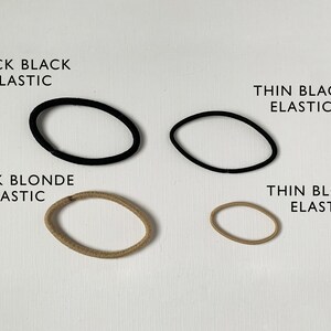 K&ouml;nnte beinhalten: Vier Haargummis in verschiedenen Farben und St&auml;rken. Zwei schwarze Haargummis, eines dick und eines d&uuml;nn. Zwei blonde Haargummis, eines dick und eines d&uuml;nn.