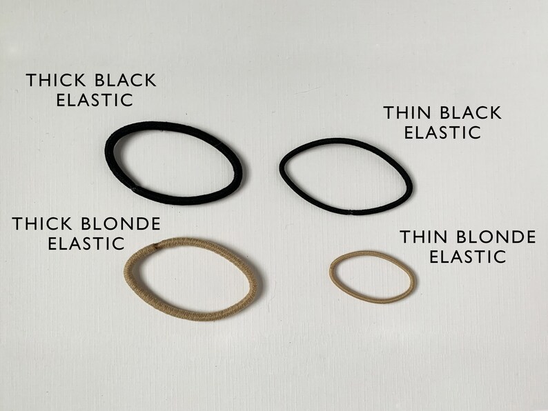 K&ouml;nnte beinhalten: Vier Haargummis in verschiedenen Farben und St&auml;rken. Zwei schwarze Haargummis, eines dick und eines d&uuml;nn. Zwei blonde Haargummis, eines dick und eines d&uuml;nn.