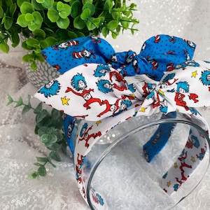 May include: A blue and white headband with a bow featuring a print of the character Thing 1 and Thing 2 from the book "The Cat in the Hat".