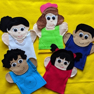 May include: Five felt hand puppets with different colored shirts and hair. The puppets have smiling faces with black eyes and brown skin.