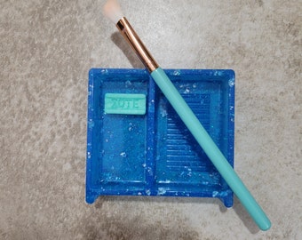 May include: A blue glitter tray with a small green soap bar that says "VOTE" and a light blue makeup brush.