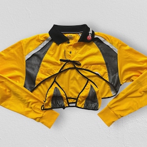 Peut inclure: Un haut à manches longues jaune vif de style polo court avec un col noir portant du texte blanc, des empiècements latéraux en maille noire et une pièce supérieure intégrée en forme de triangle jaune et noir avec de fines bretelles.