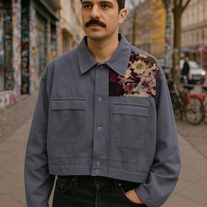 Può includere: Giacca corta blu ardesia con due tasche frontali e una toppa floreale sulla parte superiore sinistra. La toppa floreale presenta fiori bordeaux, crema e rosa. La giacca ha una chiusura con bottoni e un colletto.