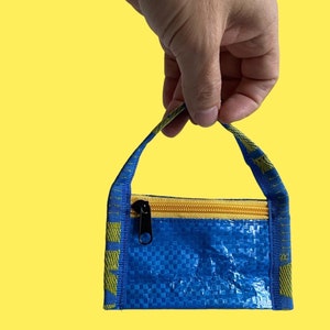 以下が含まれることがあります： 黄色いジッパーと黄色と青のストラップが付いた小さな青いジッパー付きポーチ。ポーチは織りプラスチック素材で作られています。