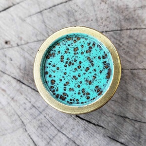 May include: A round, gold-colored knob with a turquoise blue center. The center has a swirling, marbled pattern with brown accents.