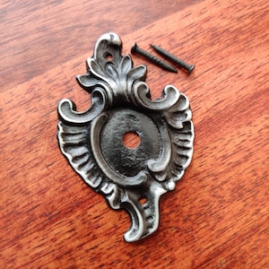 May include: A silver and black metal decorative accent with a floral design. The accent has a round hole in the centre and comes with two small black screws.