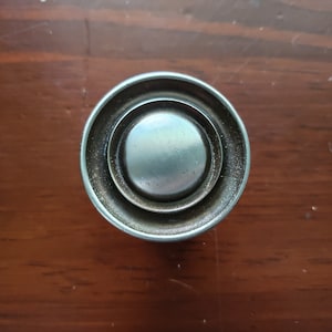 May include: A silver round cabinet knob with a concentric circle design.