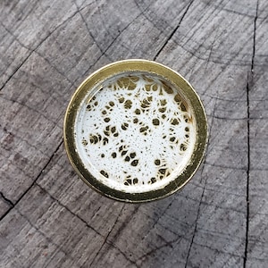 Peut inclure: Un bouchon de bouteille rond de couleur dorée avec un motif blanc en dentelle à l'intérieur.